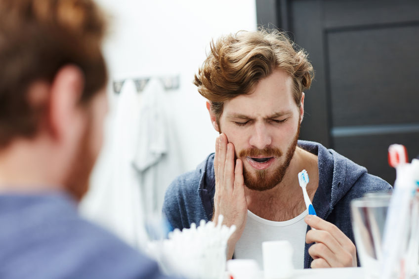 Man with toothache brushing teeth