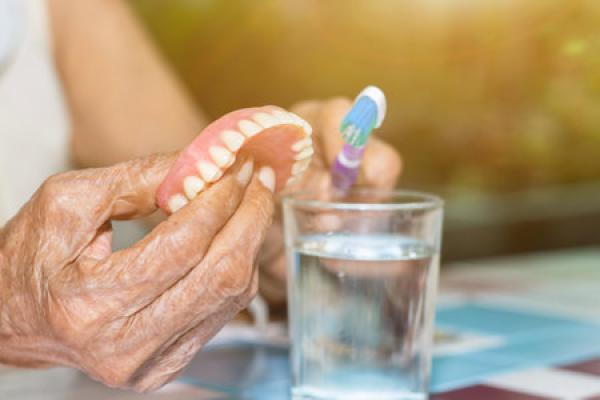 A woman holds a row of dentures and attempts to clean them with a toothbrush